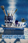 Paintbrushes and flower in cups on stack of blue books