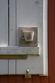 Candle lantern made from teacup embedded in concrete on window shutter