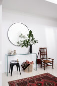 Vase of leafy branches on glass console table, stool, basket and chair in foyer