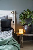 Bed with DIY headboard and houseplant on bench used as bedside table