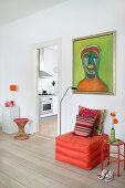 Orange pouffe below green painting in living room