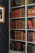 Old books on shelves next to dark blue, diamond-patterned wallpaper