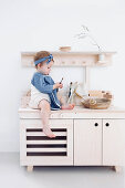Little girl sitting on pale wooden play kitchen