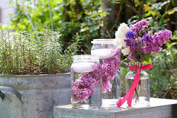 Bouquet of lilac and aquilegia next to candle lanterns made from preserving jars filled with water, lilacs and floating candles