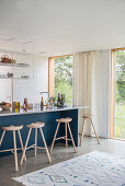 Dreibeinige Barhocker an blauer Küchentheke im offenen Wohnraum