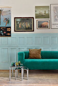 Emerald-green-sofa against pale blue panelled wainscoting below gallery of pictures