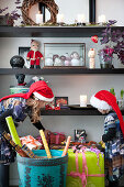 Two children wearing Christmas hats placing wrapped gifts on shelves
