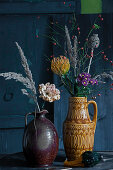 Autumn bouquets of carnations, pincushion, chrysanthemums, rose hips, poppy seed heads and grass seed heads in vintage jugs