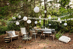 Table and chairs and further seating amongst party decorations in woodland clearing