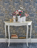 Flowers on console table against vintage-style floral wallpaper