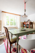 Various chairs around old table in dining room with tiled walls