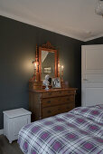 Antique chest of drawers with mirror against dark wall in bedroom