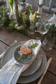 Place setting decorated with heart-shaped biscuit and eucalyptus sprig on set table