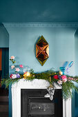 Golden sculpture on blue wall above fireplace with kitschy garland