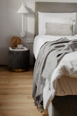 Nachttisch und Wandlampe neben Bett mit weißer Bettwäsche