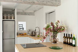 Yellow sand coloured concrete work surfaces in kitchen with vase of flowers and fridge