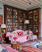 Pink throw on sofa in front of tall, antique bookcase