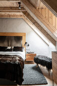 Luxurious double bed and stool with fur cover in bedroom with wooden ceiling and skylight