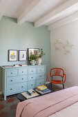 Pale blue chest of drawers against duck-egg-blue wall in bedroom with white ceiling beams