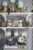 Crockery on shelves on wall with patterned wallpaper in country-house kitchen