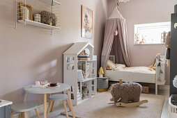 Dolls' house and bed with canopy in girl's bedroom with matt pink walls