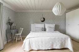 White wardrobe, double bed and desk in bedroom with patterned wallpaper
