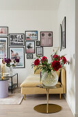 Glass vase of red peonies, sofa and gallery of photographs on wall of living room
