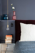 Nachttisch und Pendelleuchte neben Doppelbett vor grau gestrichener Wandnische