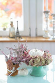 White pumpkins with a wreath of hydrangea flowers and pink pepper, budding heather in a pot with a maple leaf