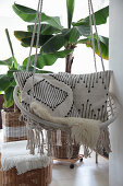 Scatter cushions with ethnic patterns in hanging chair in front of banana trees planted in baskets