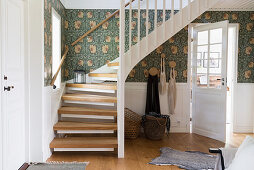 An entrance hall with wooden stairs, white cassette cladding and wallpaper