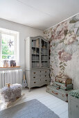 A grey dresser and a stack of suitcases in front of a floral wallpaper in a girl's room