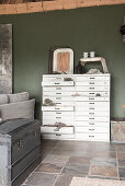 A shabby-chic style chest of drawers against a green wall