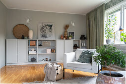 Helles Polstersessel im Wohnzimmer mit grauem Highboard vor grauer Wand