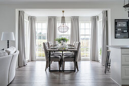 A dining area with upholstered chairs in front of French doors with curtains