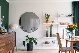 Sideboard in front of a green wall, round mirror and open shelf in the dining room