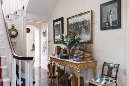 Bücherstapel auf neoklassizistischem, vergoldetem Tisch, darüber Bilder in der Eingangshalle