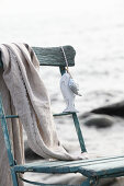 Fish-shaped pendant and cloth hanging on weathered wooden chair on beach