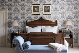 Antique wooden bed in classic bedroom with blue-and-white wallpaper