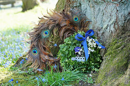 Boxwood wreath with a blue bow and flowers next to a wreath of peacock feathers