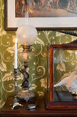 Antike Tischlampe und Kerzenhalter auf Holztisch vor grüner Tapete