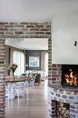 Brick fireplace next to open doorway in brick wall with view of round table and transparent chairs