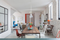 Essbereich mit verschiedenen Stühlen vor weiß gestrichener Ziegelwand in offenem Wohnraum