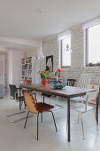 Essbereich mit verschiedenen Stühlen vor weiß gestrichener Ziegelwand in offenem Wohnraum