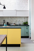 Kitchen island with yellow front in open-plan kitchen with white-painted brick wall
