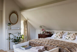 Doppelbett mit Felldecke, Kleiderbank, Kaminsims und Vase mit Blätterzweig im Dachzimmer