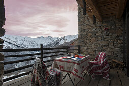 Dining table and two chairs on balcony with stone wall and view of mountain landscape