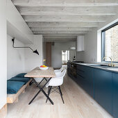Blue base units, dining table and wood-beamed ceiling in modern, open-plan kitchen