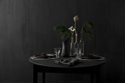 Black table set for dinner and decorated with larch branches against black wall