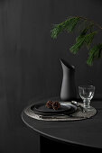 Black table set for dinner and decorated with larch branches against black wall